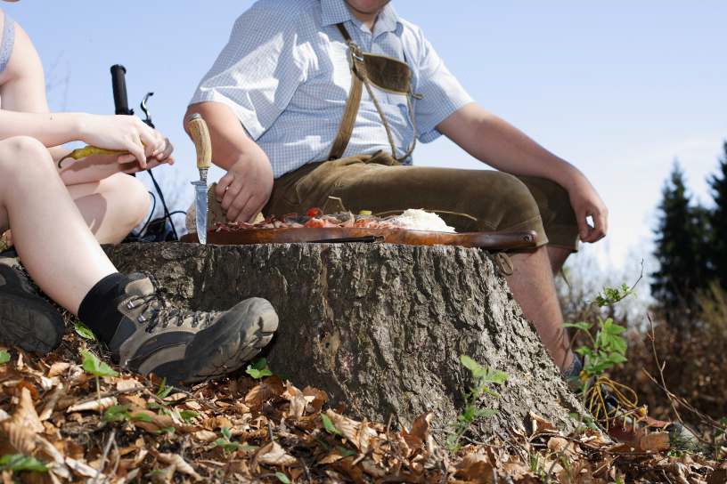 Zwei Wanderer in Lederhosen und Wanderschuhen mit schmackhafter Brettljause.