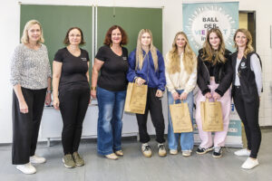 Eine Gruppe von Frauen und Mädchen posiert vor einer Tafel und einem Banner mit der Aufschrift "Ball der Vielfalt". Sie halten Papiertüten mit Logos von "Soziale Projekte Steiermark".