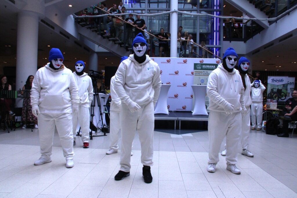 Tanzgruppe in weißen Outfits, Masken und blauen Hauben bei einer Choreografie am Inklusionstag.“